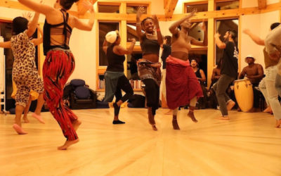 A group of dancers jump and raise their arms in an African dance class with Nkoula Badilla.