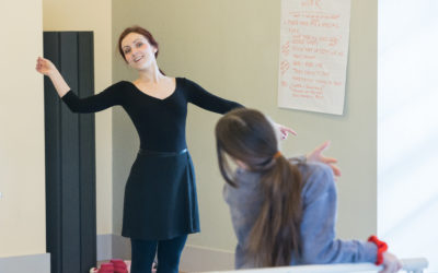 A ballet teacher gestures and leans to demonstrate.
