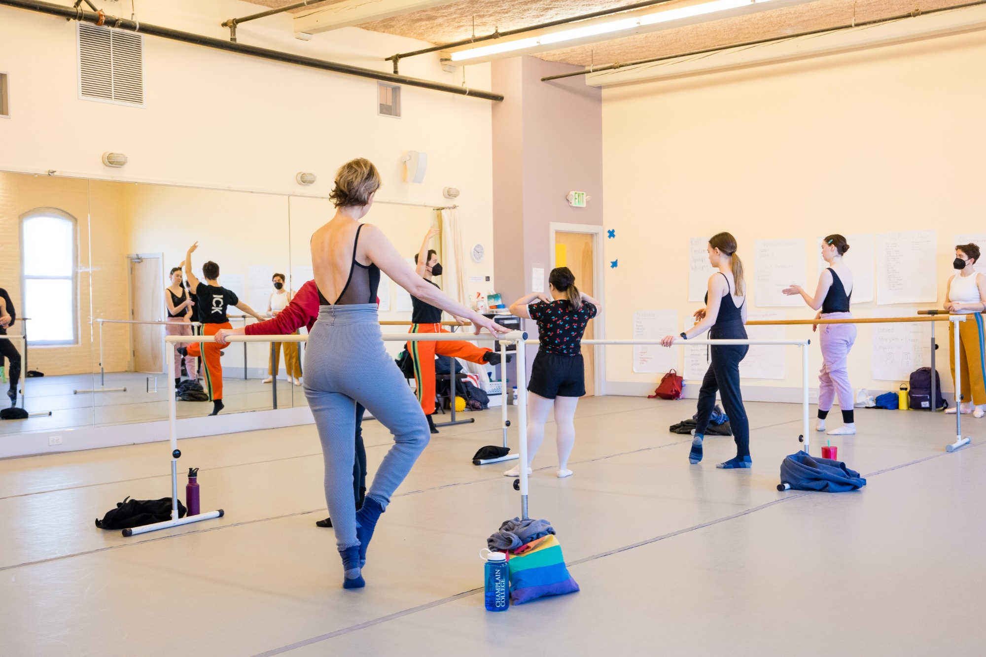 A group of students at barre in a ballet class watch the instructor demonstrate.
