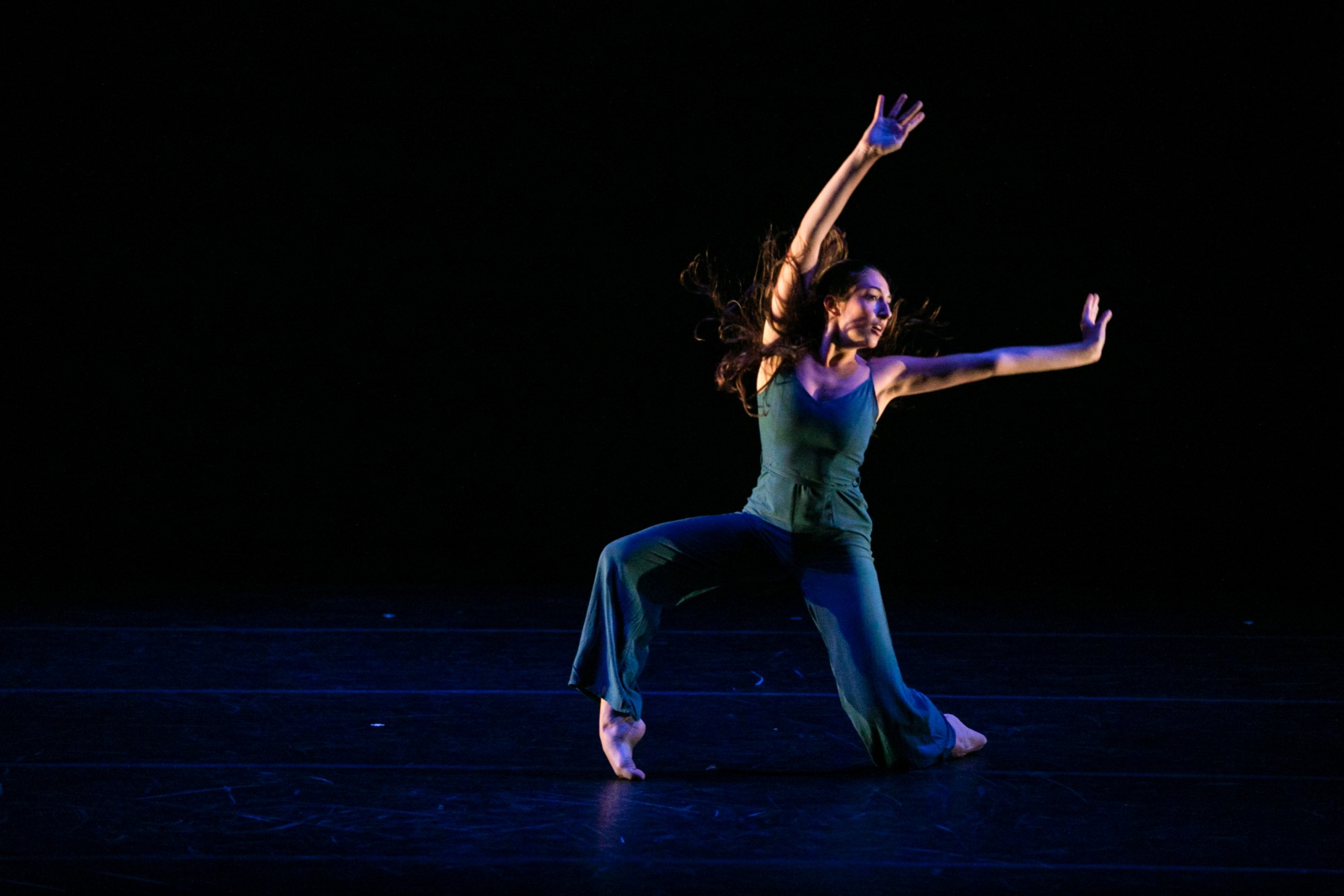 A dancer wearing a blue jumpsuit reaches as she falls to the floor.