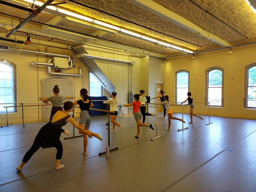A dance instructor teaching a group of dancers at ballet barres