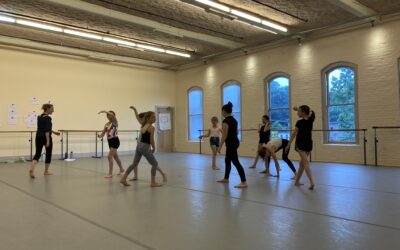 A group of dancers walking the space of a dance studio with their instructor