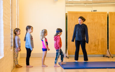 A teacher with young children in a dance studio with a tumbling mat