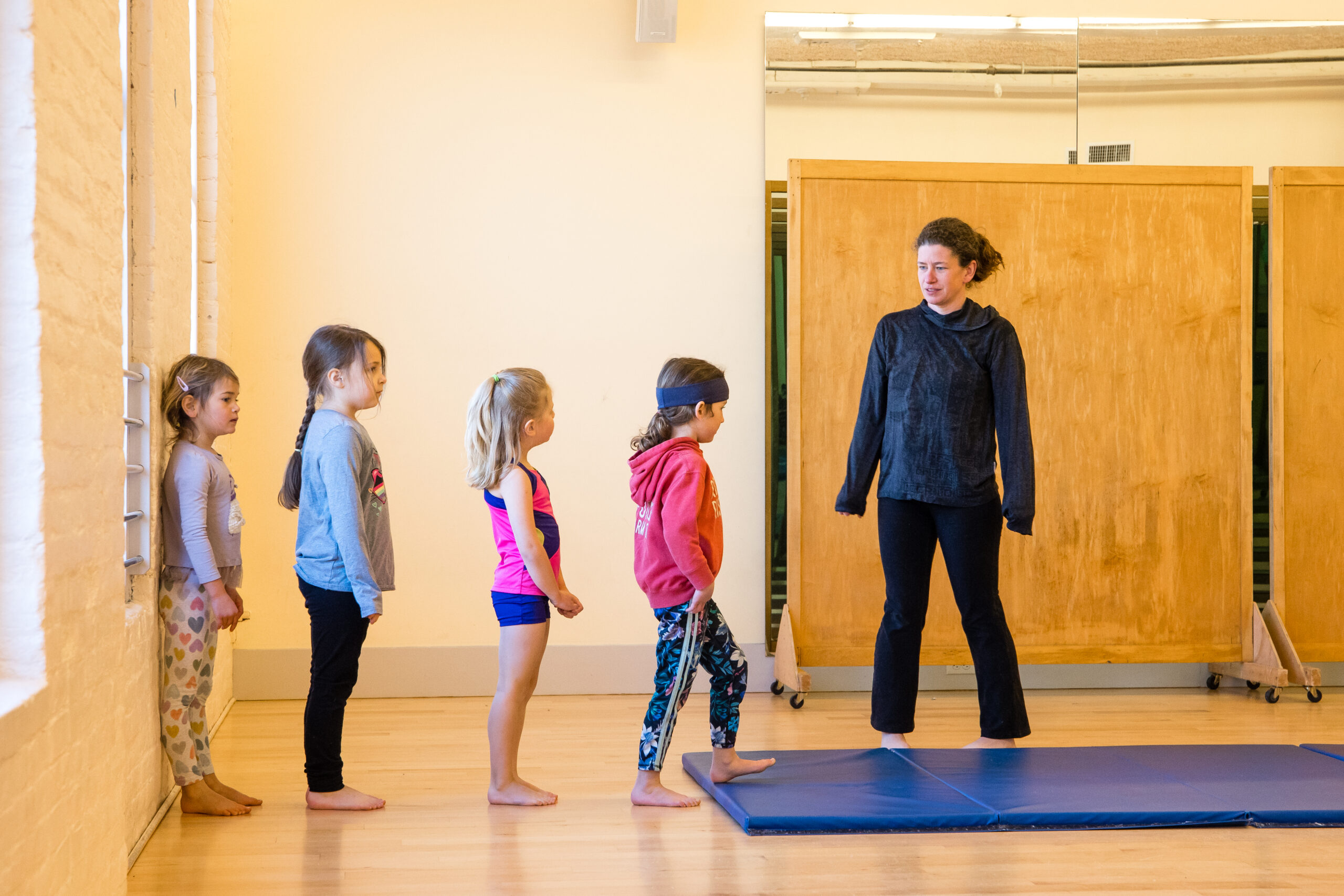 A teacher with young children in a dance studio with a tumbling mat