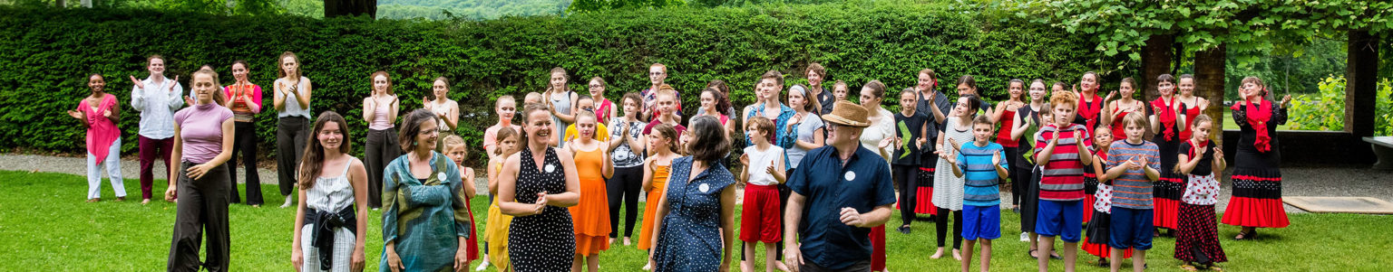 Berkshire Pulse teaching artists, staff, and dancers stand outside after a performance. Everyone is wearing colored clothing, which contrasts the greenery.