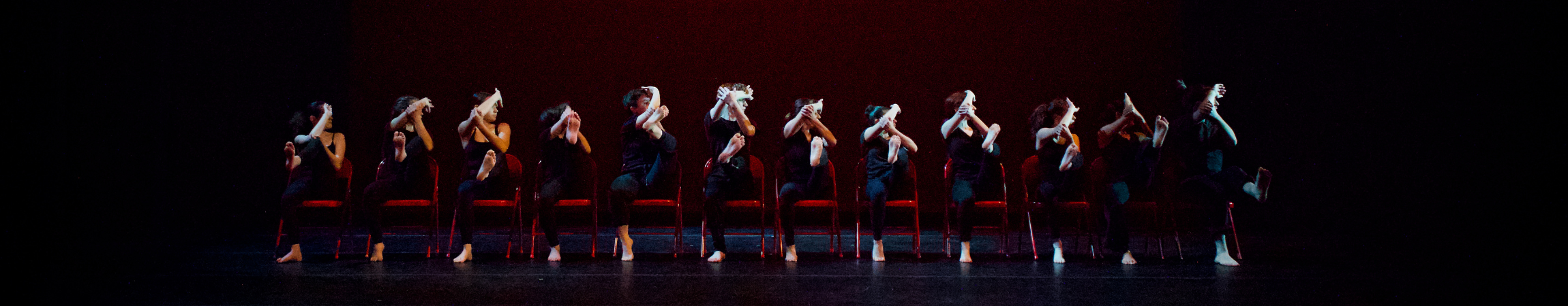 A group of dancers in a row with red chairs.