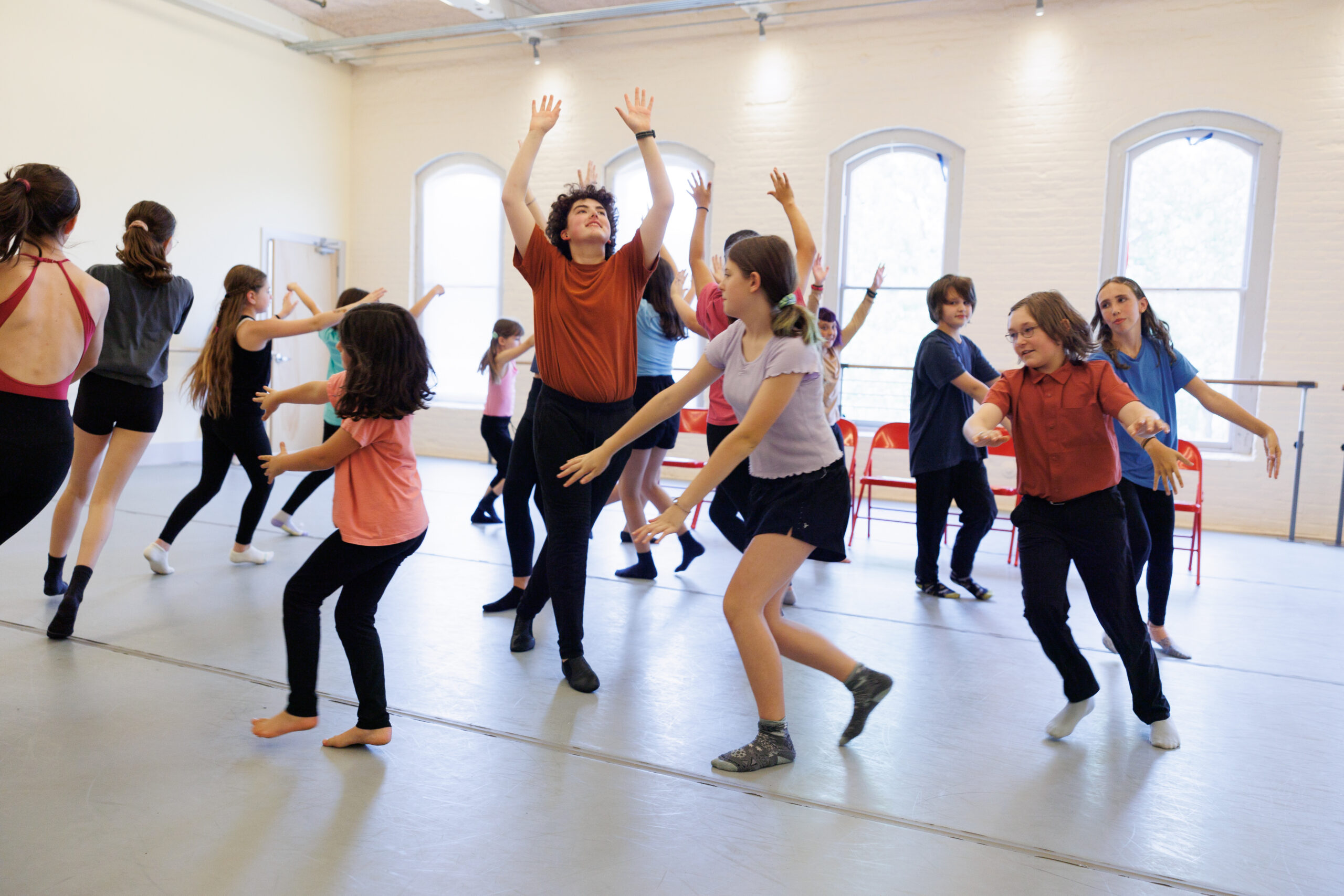 A group of youth dancers travel in a circle around a central dancer who raises his arms and gaze to the sky.